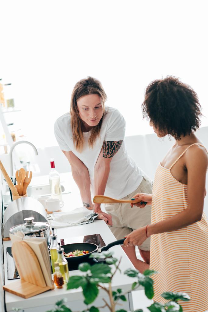Молодой человек смотрит, как африканская американская подруга готовит на кухне
  - Фото, изображение
