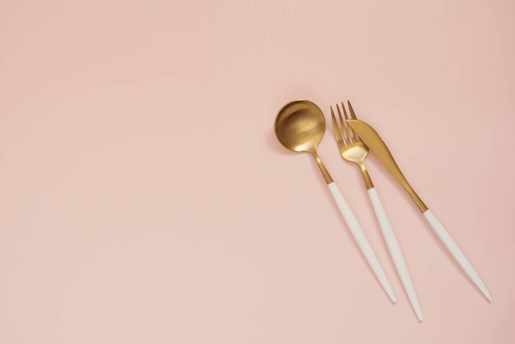 Cubiertos de oro. Conjunto de cucharas doradas, cuchillo dorado, cuchara y tenedor sobre la mesa. Cuchara de lujo set top of view. Pastel punzante fondo rosa
 - Foto, Imagen