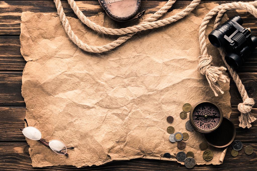 top view of blank crumpled paper with compass, binoculars and rope on rustic wooden surface - Photo, Image