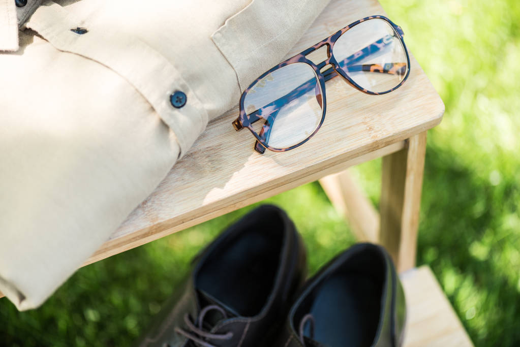 επιλεκτική εστίαση τοποθετημένα γυαλιά, δερμάτινα υποδήματα και Ανδρικό πουκάμισο σχετικά με τις ξύλινες σκάλες σε χορτολιβαδικές εκτάσεις  - Φωτογραφία, εικόνα