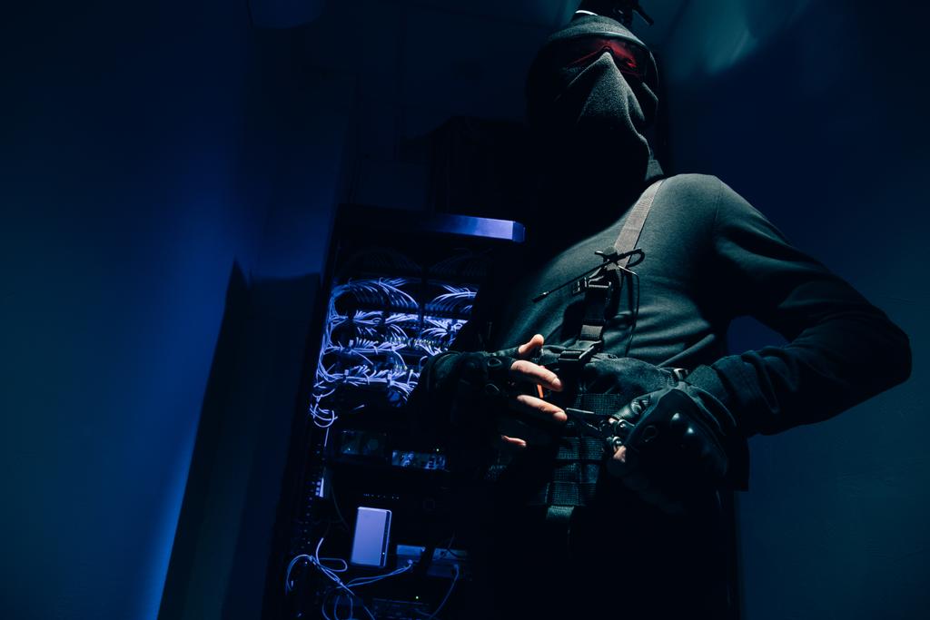 Tiefansicht des Hackers in schwarzer Kleidung und Brille mit verschiedenen Kabeln im Hintergrund - Foto, Bild
