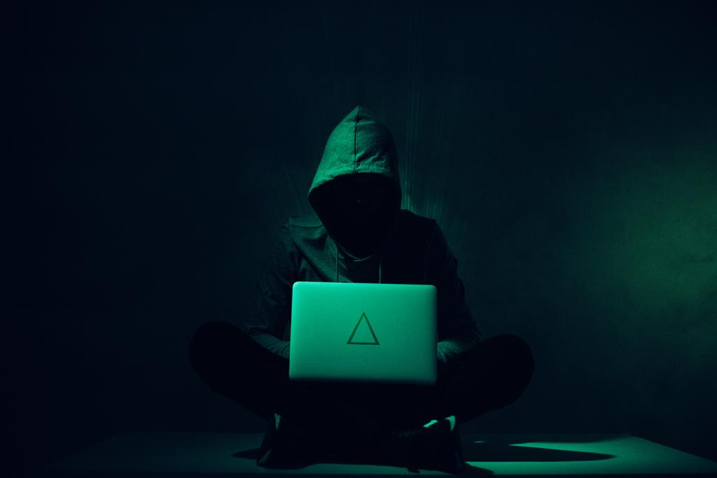 getinte foto van silhouet van hacker in hoodie met behulp van laptop - Foto, afbeelding