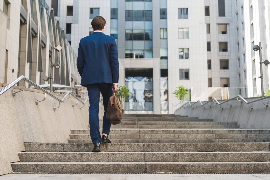 rear view of businessman in stylish suit with leather briefcase going up stairs - Photo, Image