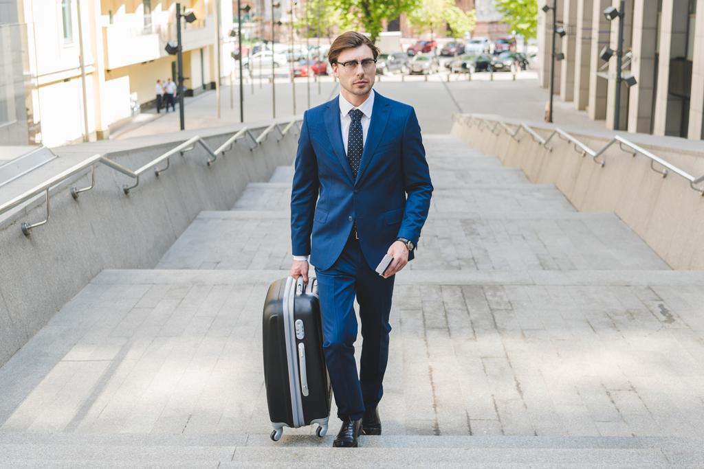 jonge zakenman in stijlvol pak met bagage en vlucht tickets - Foto, afbeelding