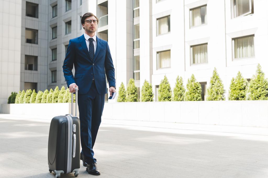 jovem empresário atraente em terno elegante com bagagem andando pelo distrito de negócios
 - Foto, Imagem