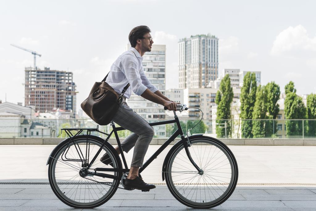 a fiatalember az elegáns ruhákat, vintage kerékpár lovaglás a város utcai oldalnézete - Fotó, kép