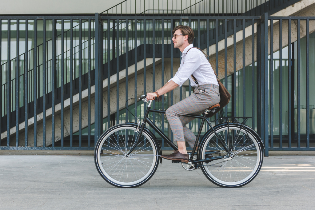 Вид сбоку красивого молодого человека, катающегося на винтажном велосипеде по городской улице
 - Фото, изображение
