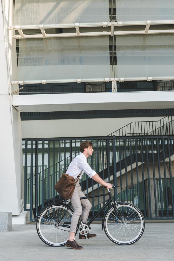 Вид сбоку стильного молодого человека, катающегося на винтажном велосипеде по городской улице
 - Фото, изображение