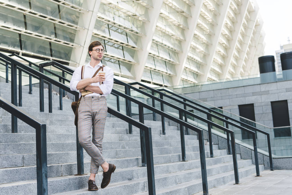 attraente giovane uomo in piedi sulle scale di fronte allo stadio con libro e caffè per andare
 - Foto, immagini