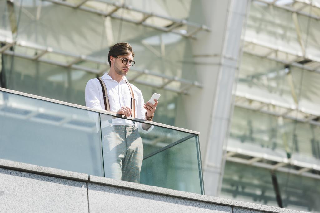 bottom view of handsome young man using smartphone on balcony in front of stadium - Photo, Image