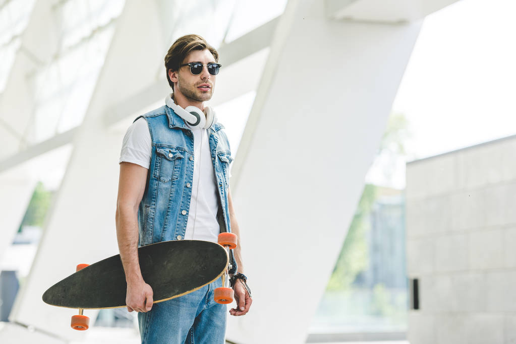 Stylový mladé bruslaře v džínové oblečení s longboard a sluchátka - Fotografie, Obrázek