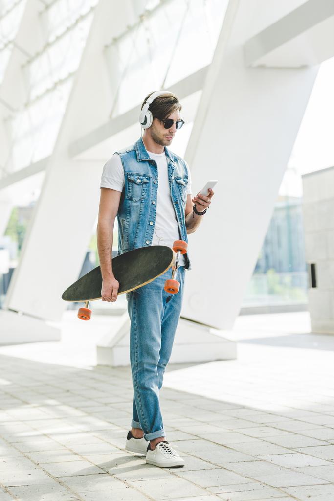 stylish young man with skateboard using smartphone on street of modern city - Photo, Image