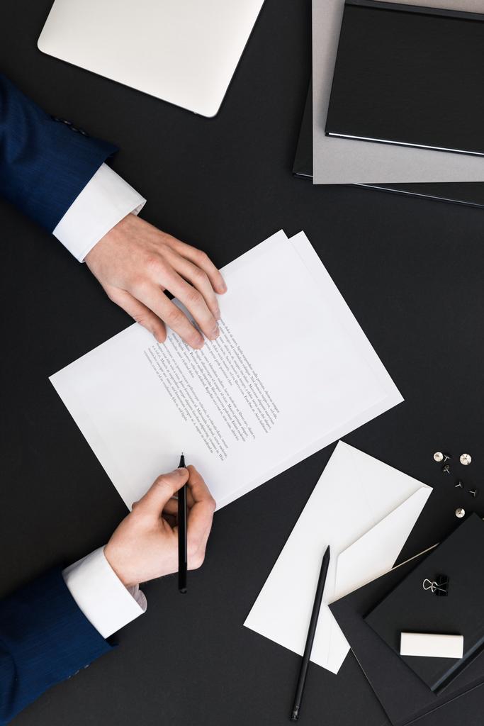 Teilansicht eines Geschäftsmannes im Anzug beim Unterschreiben von Papieren am Arbeitsplatz mit Laptop - Foto, Bild