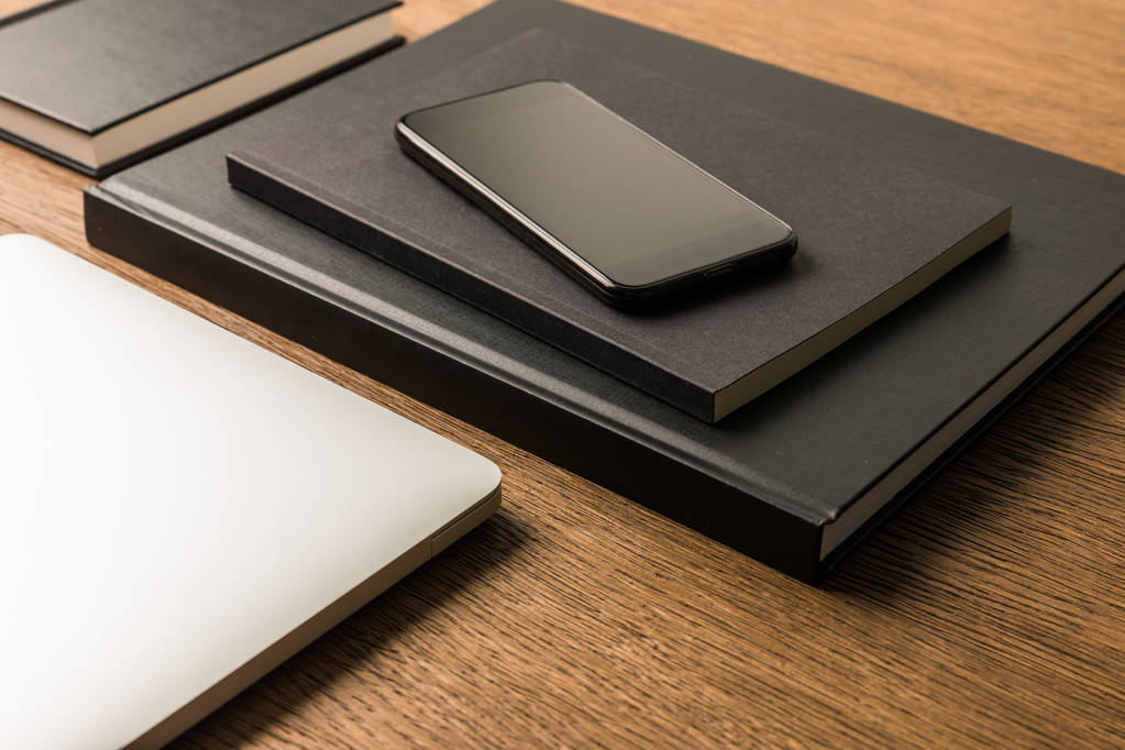 close up view of laptop, pile of black notebooks and smartphone on wooden tabletop - Photo, Image
