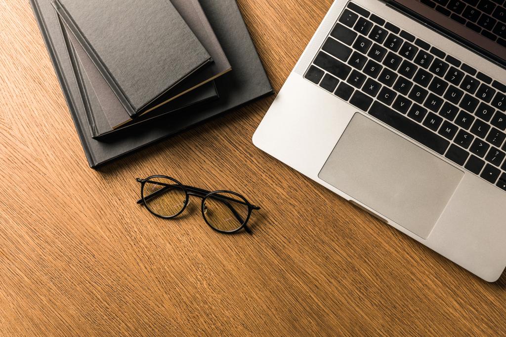 pohled shora uspořádány hromadu černý zápisník, laptop a brýle na dřevěnou desku - Fotografie, Obrázek