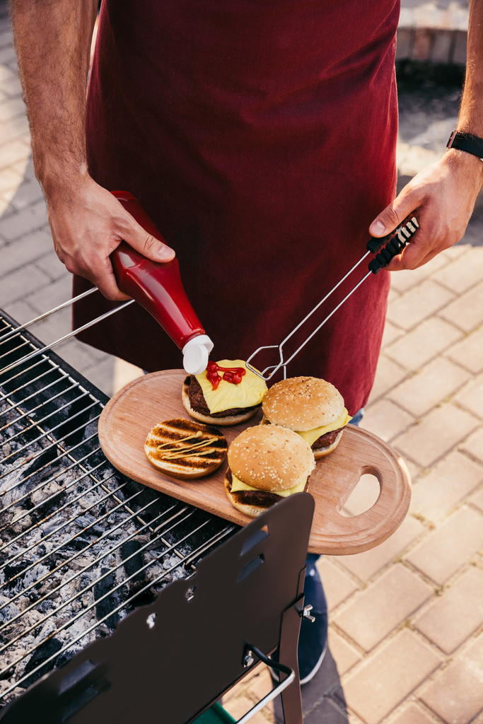 Chef adicionando ketchup para hambúrgueres grelhados para churrasco ao ar livre
 - Foto, Imagem
