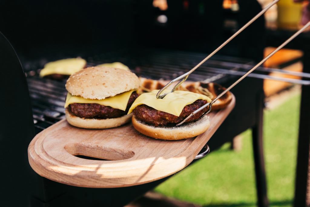 Serve pinze che tengono hamburger caldi alla griglia per barbecue all'aperto
 - Foto, immagini
