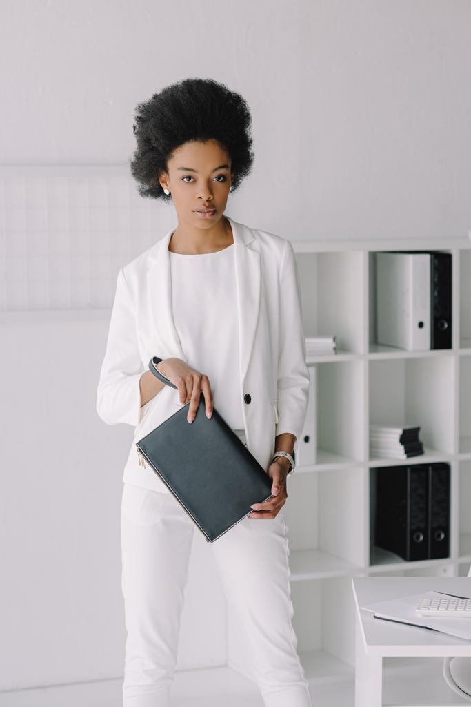 atractiva mujer de negocios afroamericana sosteniendo pequeña bolsa en la oficina
 - Foto, Imagen