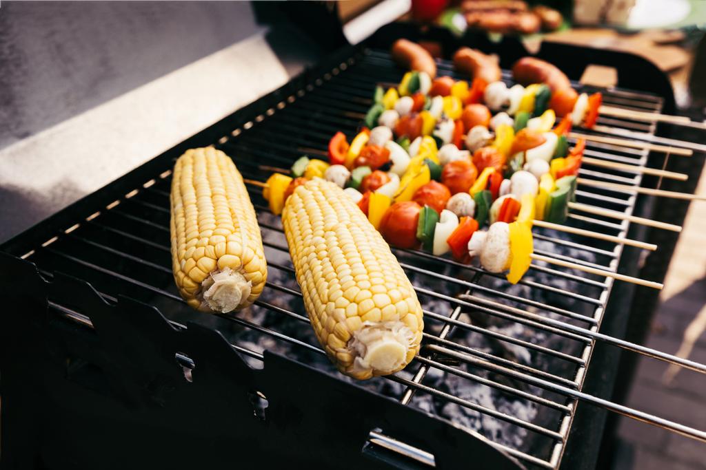 Corn cobs and vegetables on skewers cooked outdoors on grill - Photo, Image