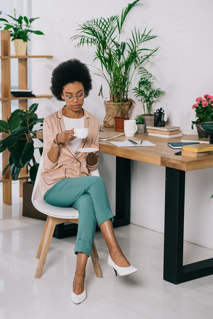 attractive african american businesswoman holding cup of coffee in office - Photo, Image