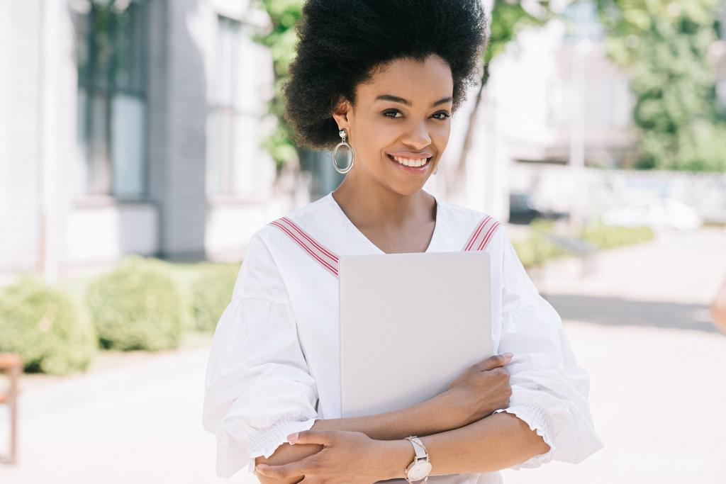 vonzó mosolygó afro-amerikai üzletasszony állva street, laptop - Fotó, kép