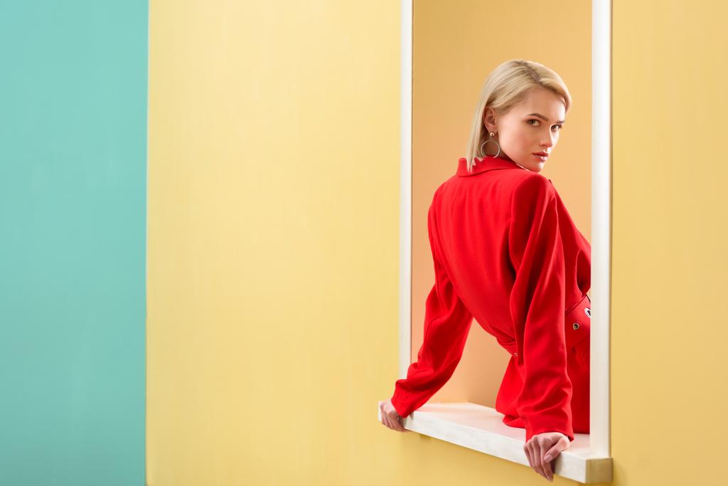 νέα μοντέρνα γυναίκα σε κόκκινο κοστούμι κοιτάζοντας διακοσμητικό παράθυρο - Φωτογραφία, εικόνα