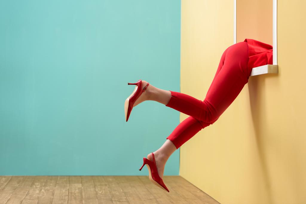 visão parcial da mulher em calças vermelhas e sapatos pendurados para fora janela decorativa
 - Foto, Imagem