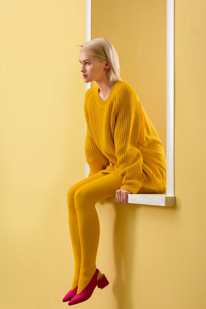 a stílusos nő sárga pulóver, rózsaszín cipő, harisnya dekoratív ablakban ül oldalnézete - Fotó, kép