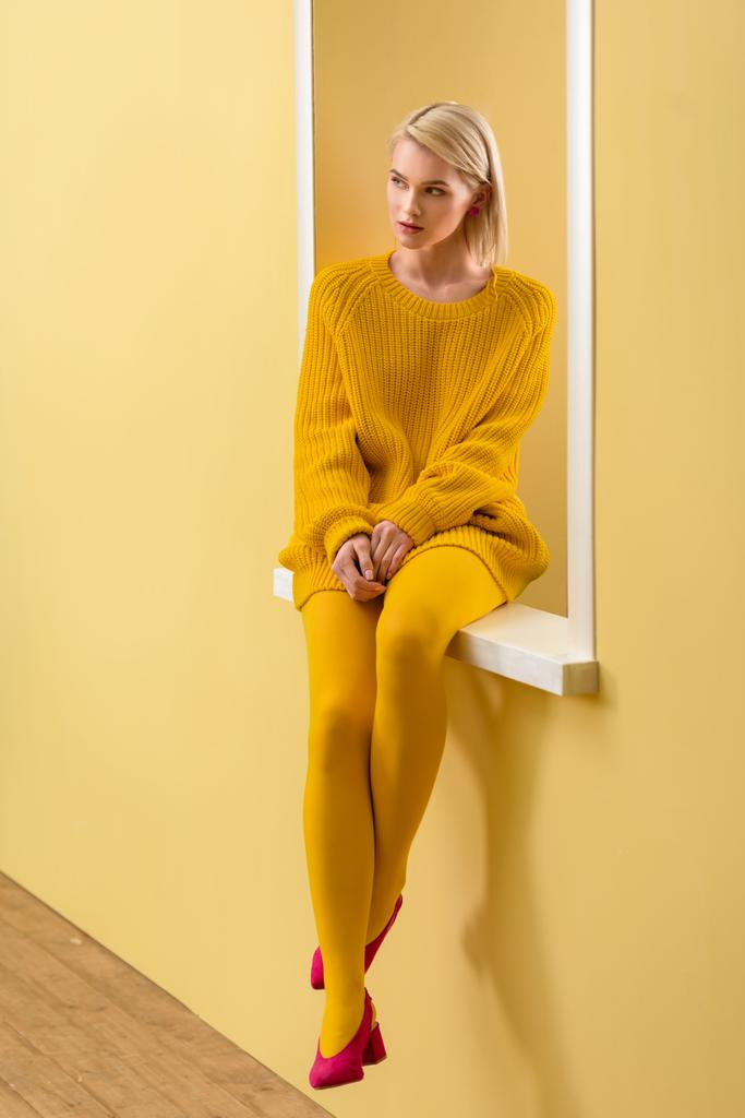 κομψή γυναίκα σκεπτικός σε κίτρινο πουλόβερ και καλσόν κάθεται στο διακοσμητικό παράθυρο - Φωτογραφία, εικόνα