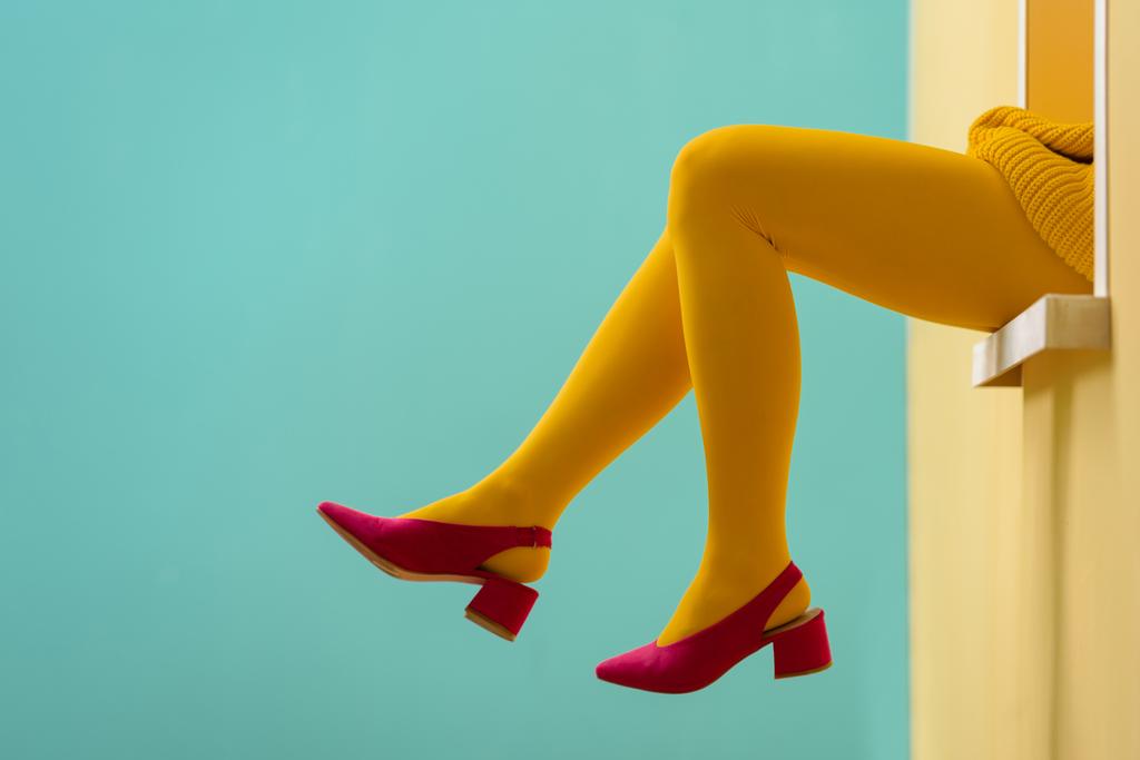 Μερική άποψη της γυναίκας στο καλσόν κίτρινο και ροζ παπούτσια σε μπλε φόντο - Φωτογραφία, εικόνα