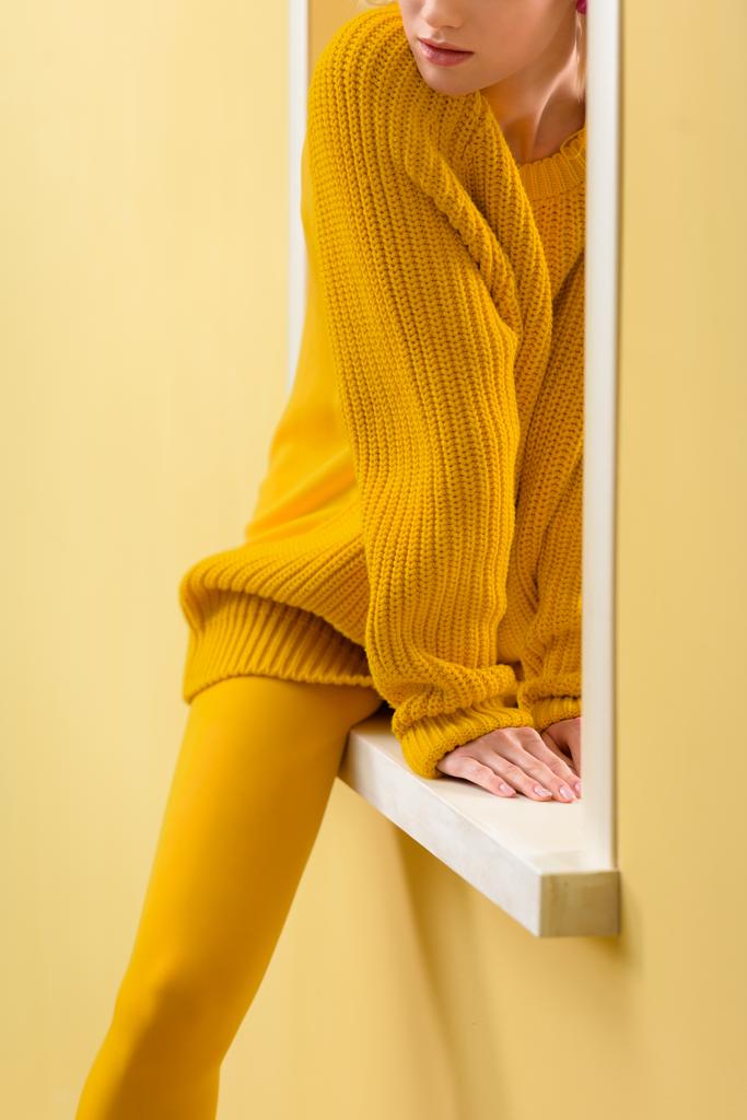 przycięte strzał stylowe kobiety w żółty sweterek i rajstopy, siedząc na dekoracyjne okno - Zdjęcie, obraz