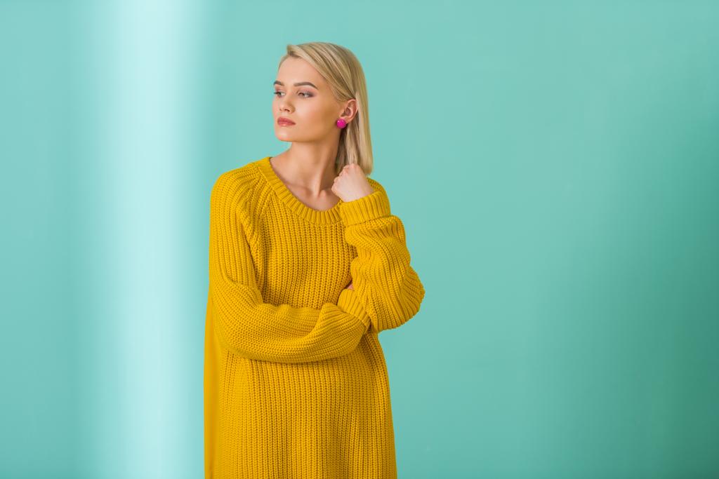 Porträt einer schönen nachdenklichen Frau in gelbem Pullover, die auf blauem Hintergrund posiert - Foto, Bild