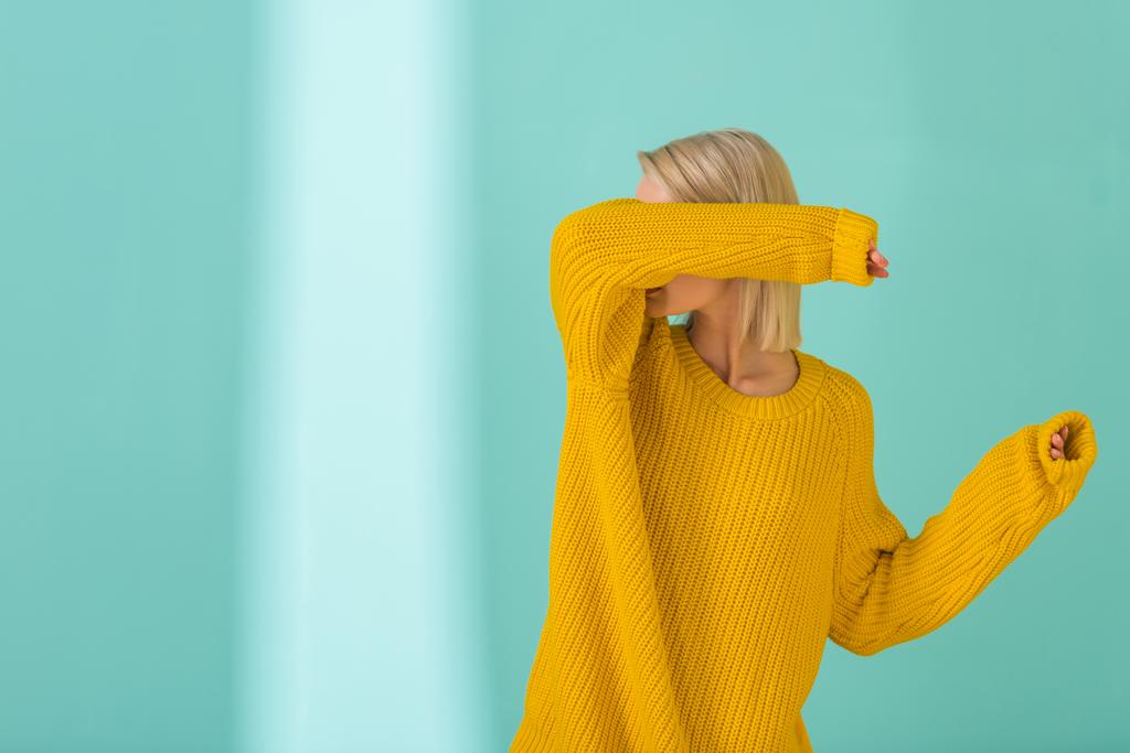 κρυμμένη άποψη της γυναίκας σε κίτρινο πουλόβερ θέτοντας σε μπλε φόντο - Φωτογραφία, εικόνα