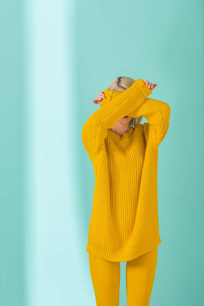 obscured view of woman in yellow sweater and tights posing on blue background - Photo, Image