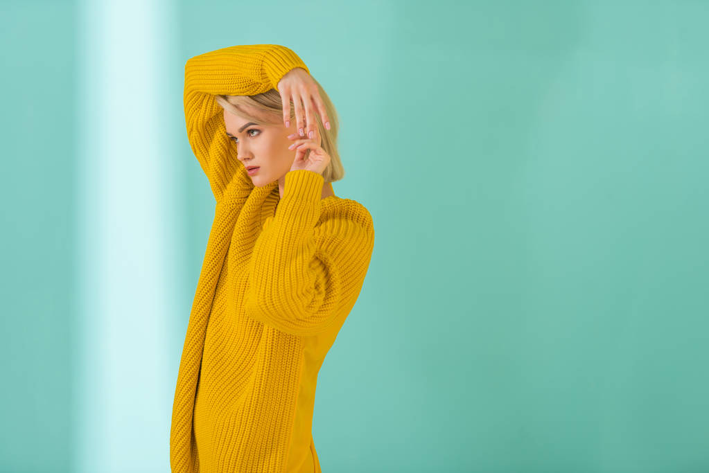 vista lateral de mujer joven en suéter amarillo posando sobre fondo azul
 - Foto, Imagen