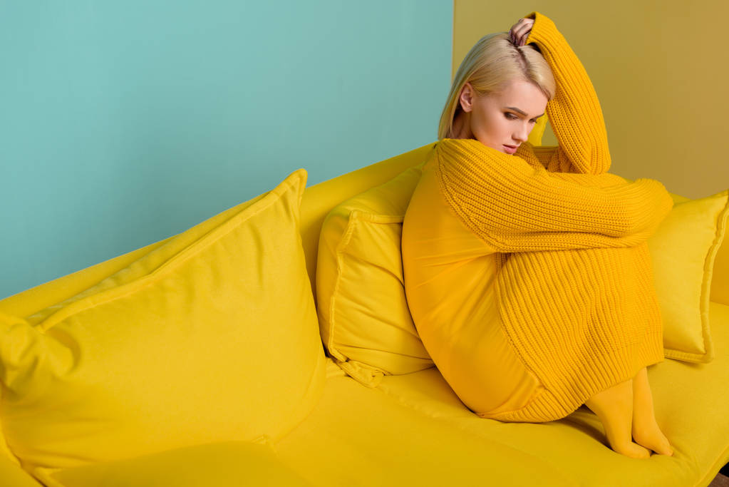 boční pohled na mladá blond žena v žlutý svetr a kalhoty sedí na měděně na modrém pozadí - Fotografie, Obrázek