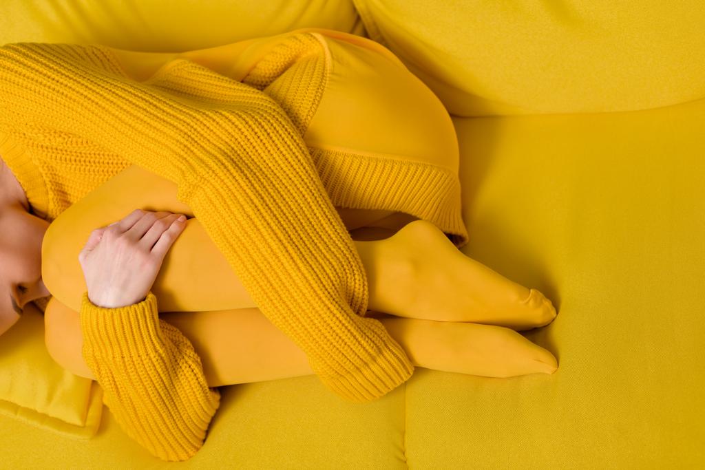Μερική άποψη της γυναίκας σε κίτρινο πουλόβερ και καλσόν στον ύπνο στον καναπέ κίτρινο - Φωτογραφία, εικόνα
