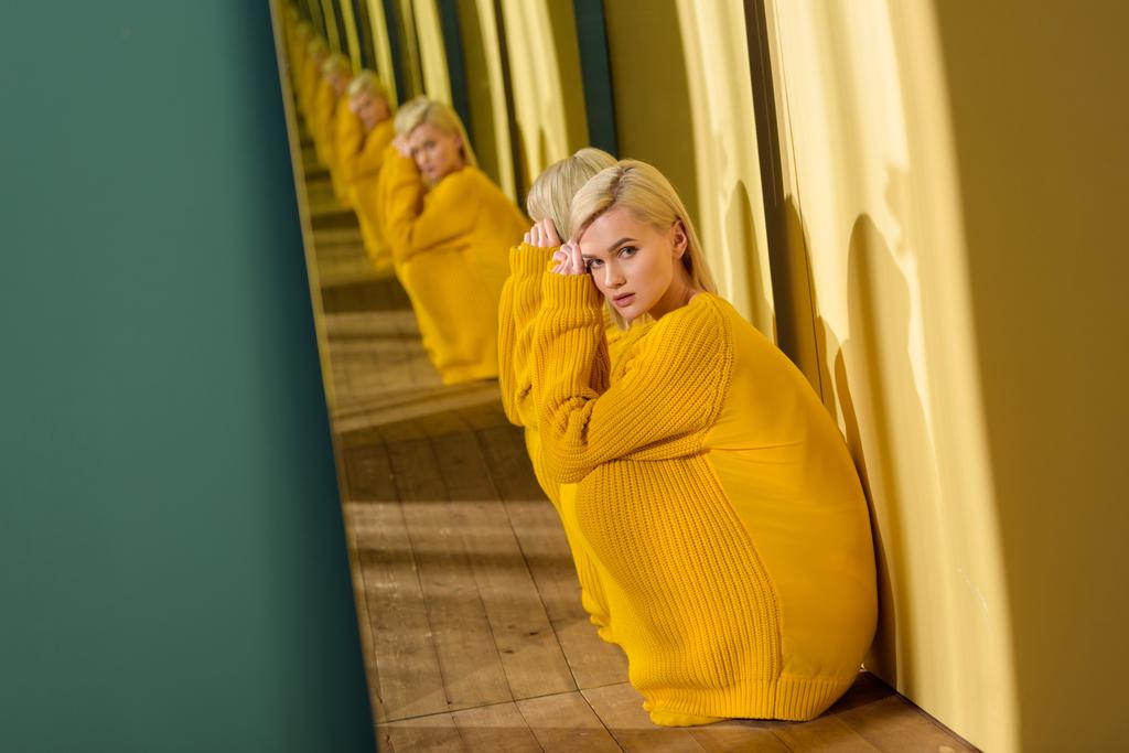 Вид сбоку красивой красивой женщины в желтом свитере, сидящей у зеркала со своим лицом
 - Фото, изображение