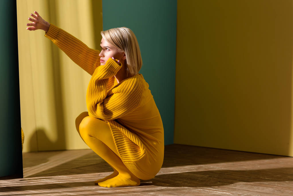 stijlvolle jongedame in de gele trui en panty's zitten op spiegel  - Foto, afbeelding