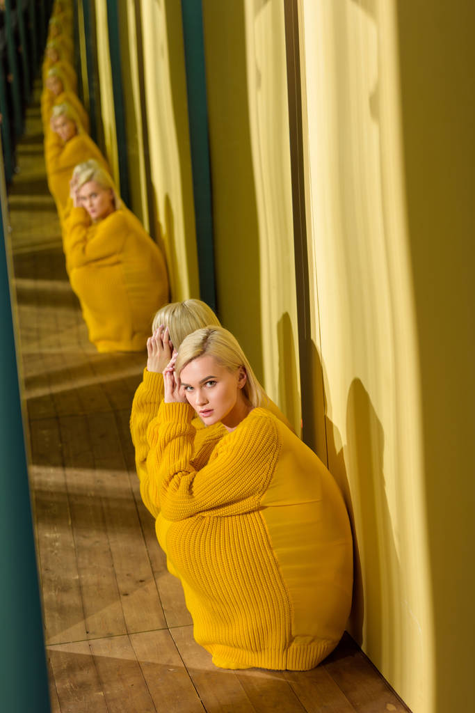 Seitenansicht der schönen jungen Frau in gelbem Pullover am Spiegel sitzend mit ihrem Spiegelbild darin - Foto, Bild