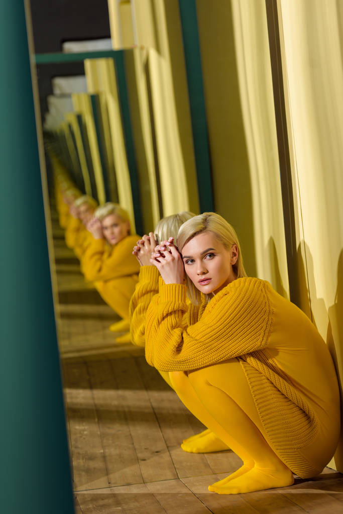 vista lateral da bela jovem mulher em suéter amarelo sentado no espelho com seu reflexo nele
 - Foto, Imagem