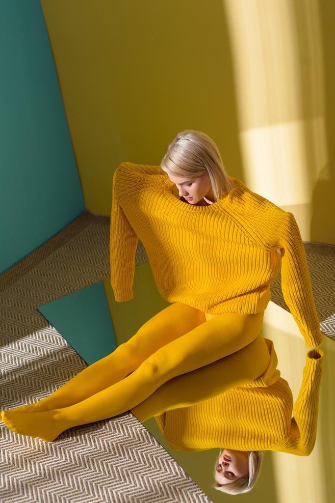 黄色いセーターやタイツで反射と鏡の上に座っての魅力的な女性のハイアングル - 写真・画像