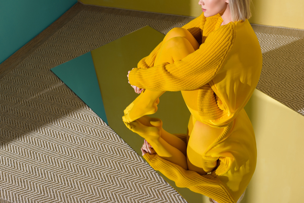 bijgesneden shot van de vrouw in de gele trui en panty's zittend op spiegel met reflectie in het - Foto, afbeelding