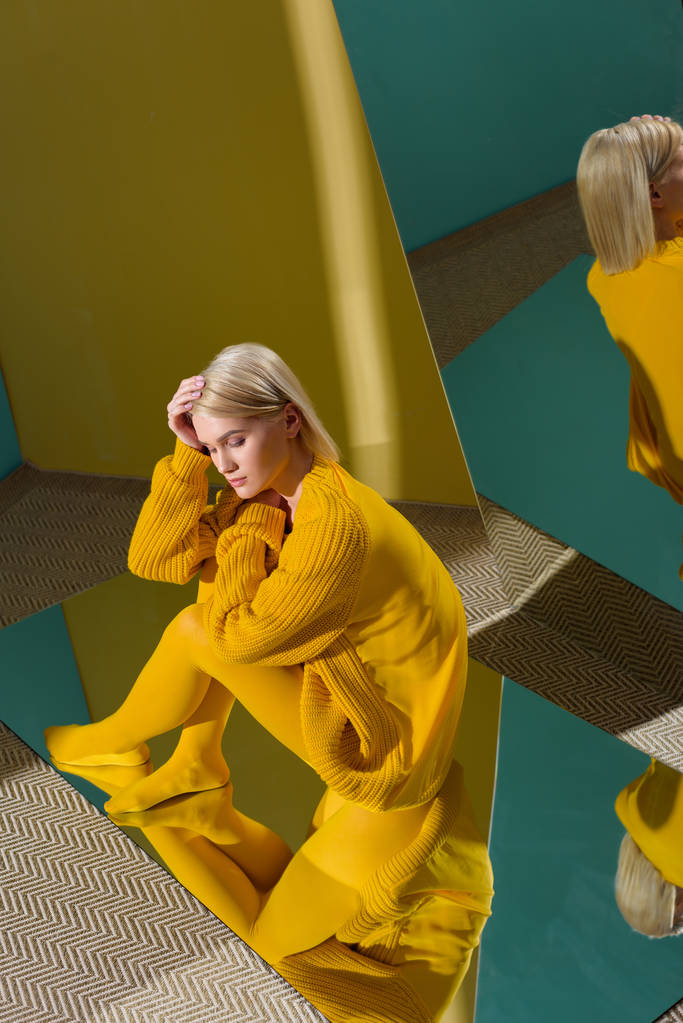 high angle view of attractive woman in yellow sweater and tights sitting on mirror with reflection in it - Photo, Image