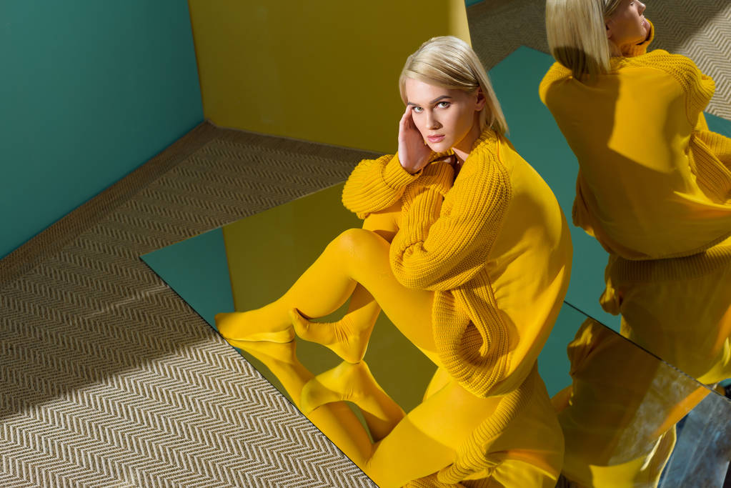 высокий угол обзора женщины в желтом свитере и колготках, сидящих на зеркале с отражением в нем
 - Фото, изображение