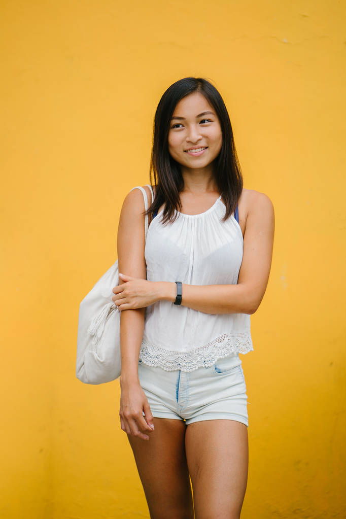 Portréja egy sportos, aranyos kínai ázsiai lány öltözött kényelmesen és mosolyogva a kamera egy stúdióban sárga háttérrel. - Fotó, kép