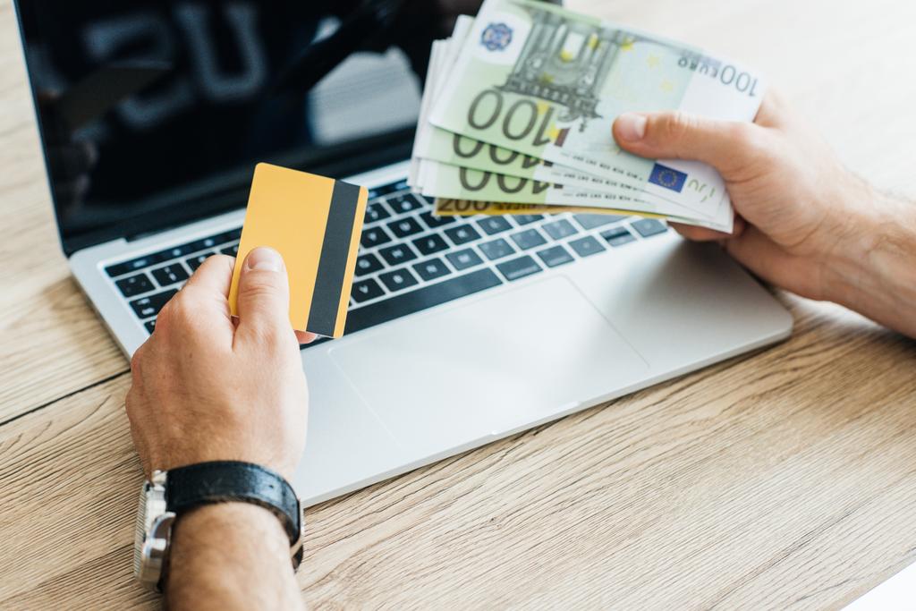 Schnappschuss von Person mit Kreditkarte und Euro-Banknoten über Laptop  - Foto, Bild