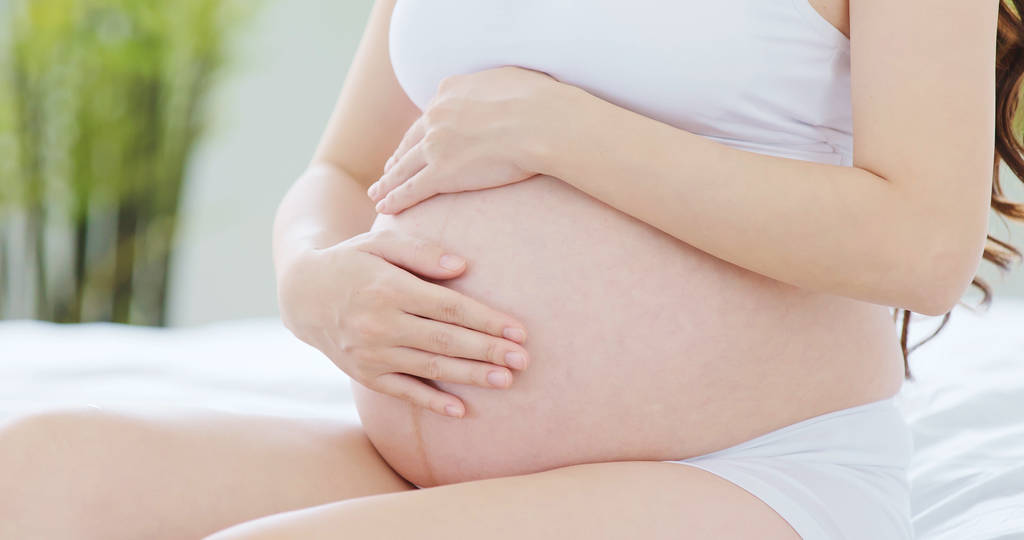 Kobieta w ciąży z brzuchem na łóżku z bliska - Zdjęcie, obraz