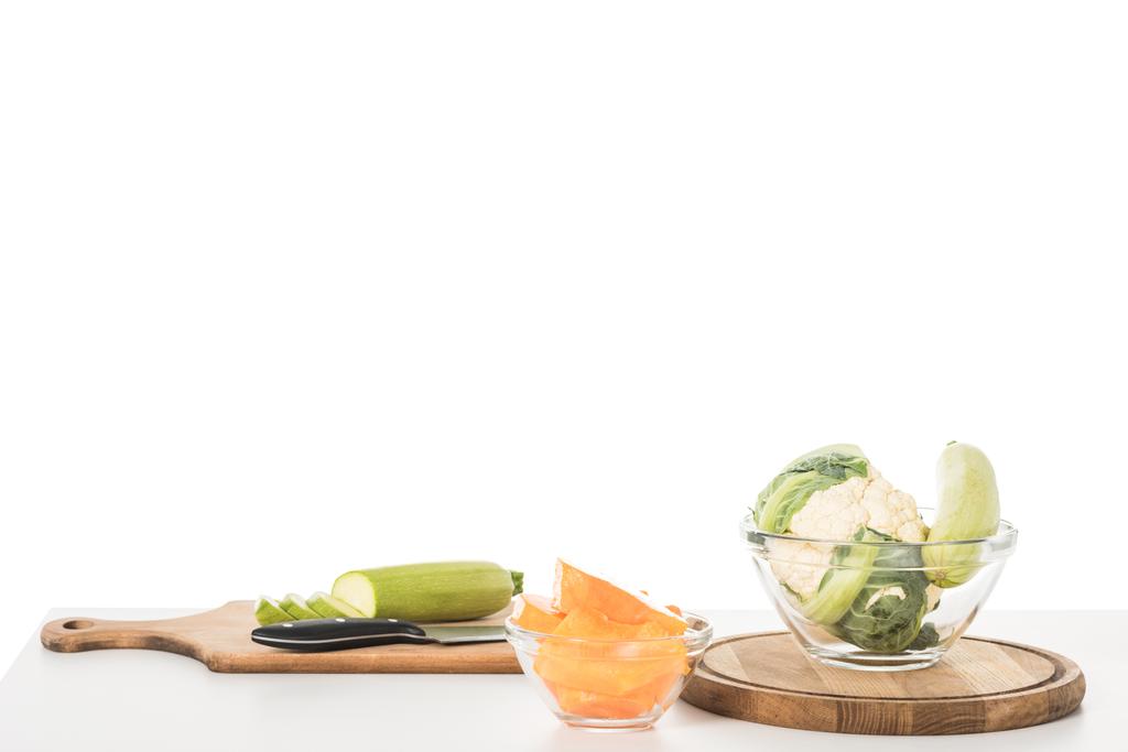 Nahaufnahme von Schneidebrettern, Messern, Schalen, Zucchinis, Kürbis und Blumenkohl auf Tisch isoliert auf weißem Hintergrund  - Foto, Bild