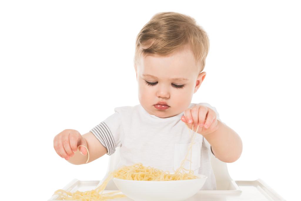 adorable niño comiendo espaguetis por las manos y sentado en trona aislado sobre fondo blanco
  - Foto, imagen